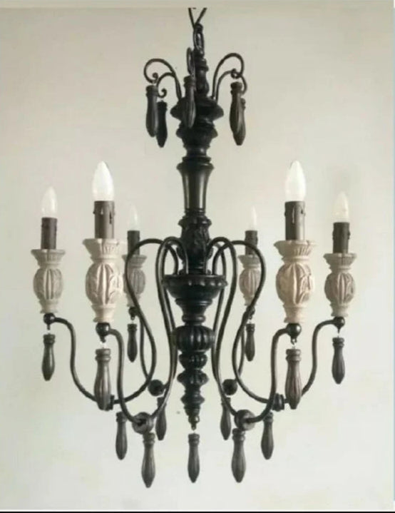 Rustic gothic-inspired wrought iron chandelier featuring carved details and flame-tip lights.