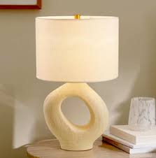 An off-white textured ceramic lamp featuring a hollow doughnut-shaped base and a classic white lampshade.