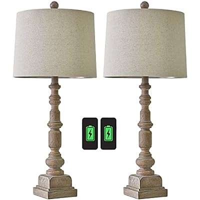 A traditional table lamp featuring a distressed, turned-wood candlestick base and a neutral beige fabric drum shade