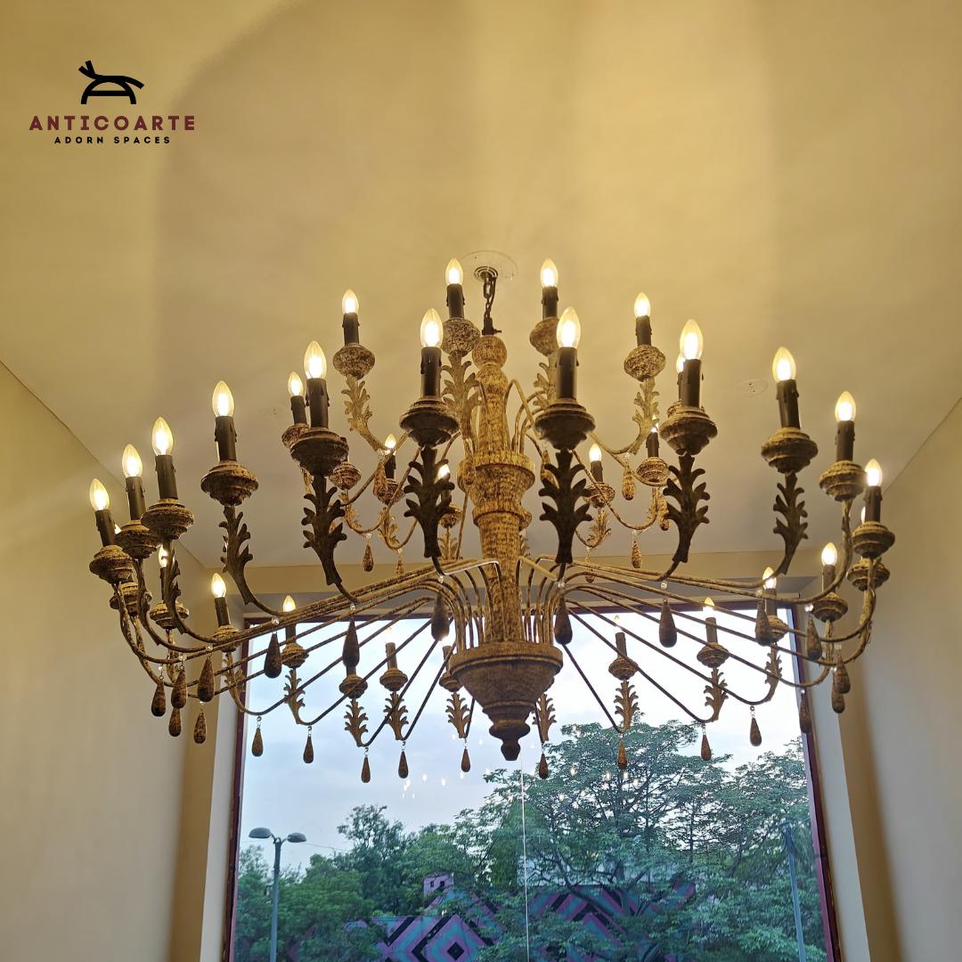 Anticoarte - Large ornate chandelier hanging in a room with a window showing trees outside.