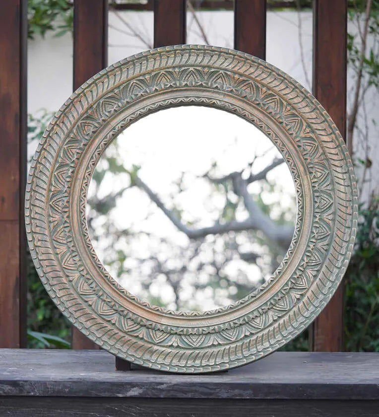 Rustic round wall mirror with an intricately carved ornate border.