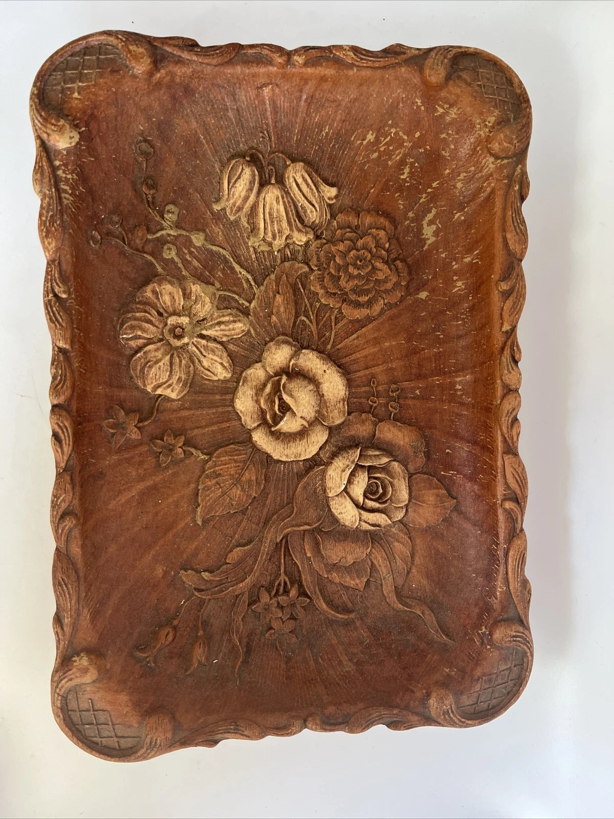 A rectangular brown wooden tray featuring a detailed, high-relief hand-carved floral arrangement of roses and bluebells in the center with a decorative wavy border.