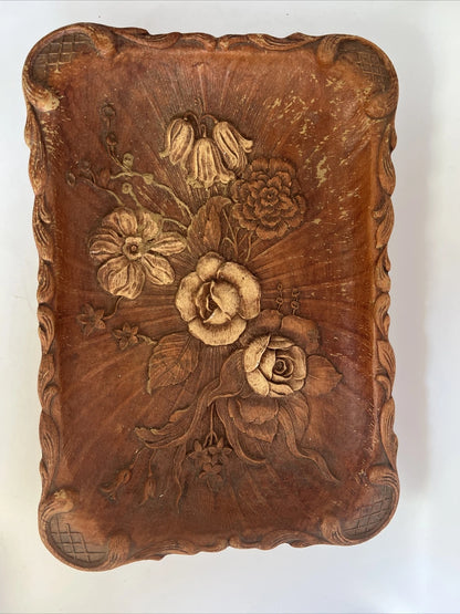 A rectangular brown wooden tray featuring a detailed, high-relief hand-carved floral arrangement of roses and bluebells in the center with a decorative wavy border.