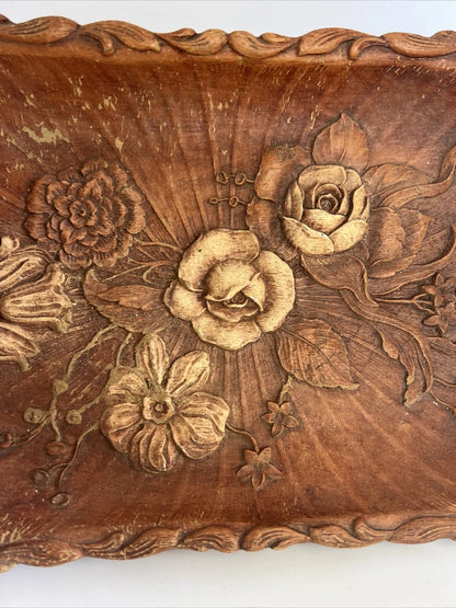 A rectangular brown wooden tray featuring a detailed, high-relief hand-carved floral arrangement of roses and bluebells in the center with a decorative wavy border.