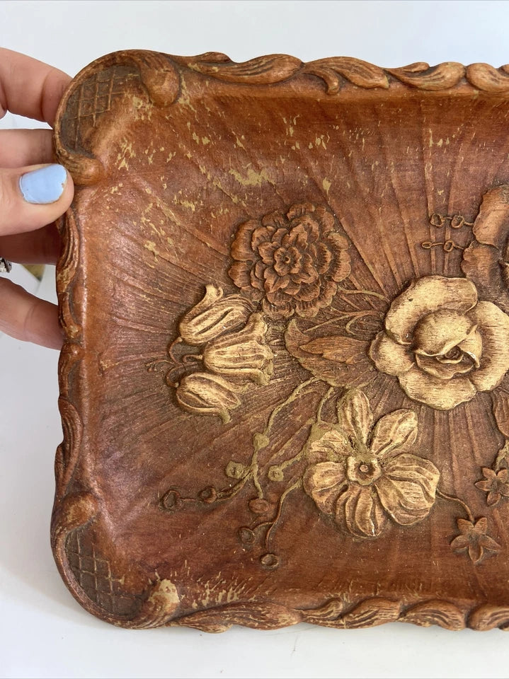 A rectangular brown wooden tray featuring a detailed, high-relief hand-carved floral arrangement of roses and bluebells in the center with a decorative wavy border.