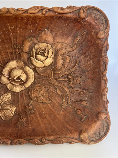 A rectangular brown wooden tray featuring a detailed, high-relief hand-carved floral arrangement of roses and bluebells in the center with a decorative wavy border.