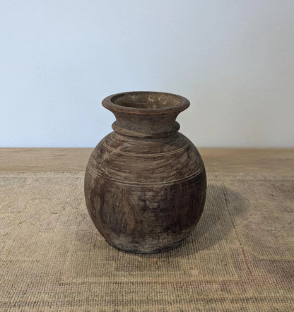 A round, dark brown rustic wooden vase