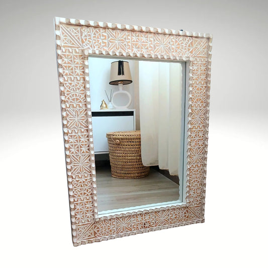 A rectangular wooden mirror frame with intricate geometric hand carvings and a light white-washed finish.