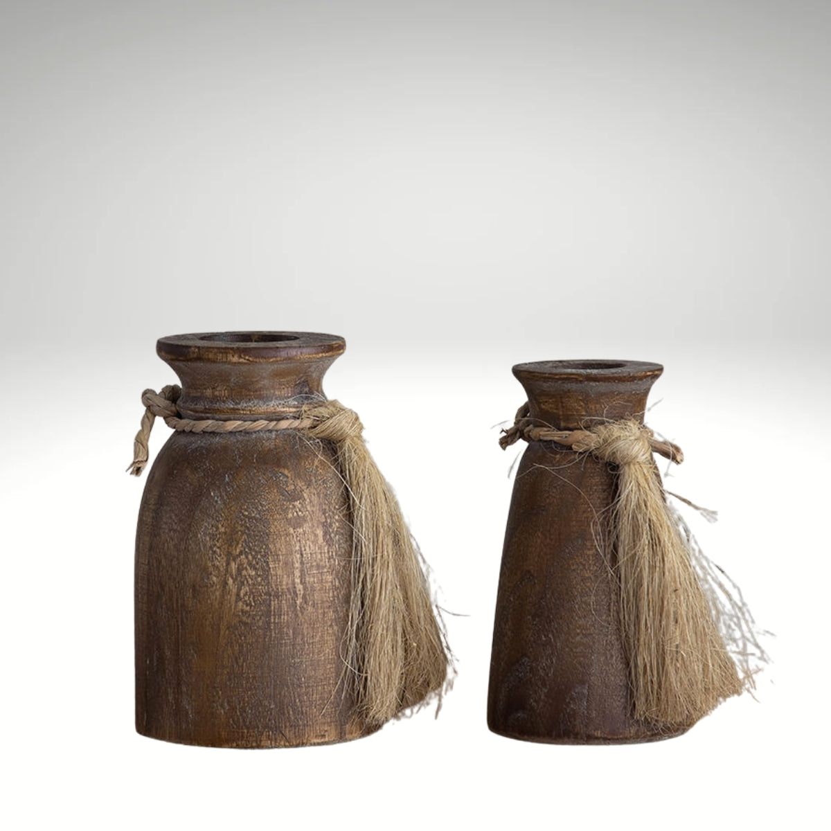 A pair of rustic brown wooden vases in different sizes, each decorated with a jute rope tassel tied around the neck.
