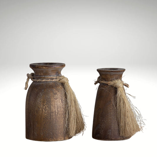 A pair of rustic brown wooden vases in different sizes, each decorated with a jute rope tassel tied around the neck.
