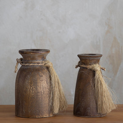 A pair of rustic brown wooden vases in different sizes, each decorated with a jute rope tassel tied around the neck.