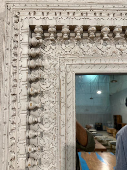 An ornate, rectangular white-washed wooden mirror frame