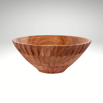 A large, fluted wooden serving bowl with a carved exterior pattern sitting on a concrete countertop.