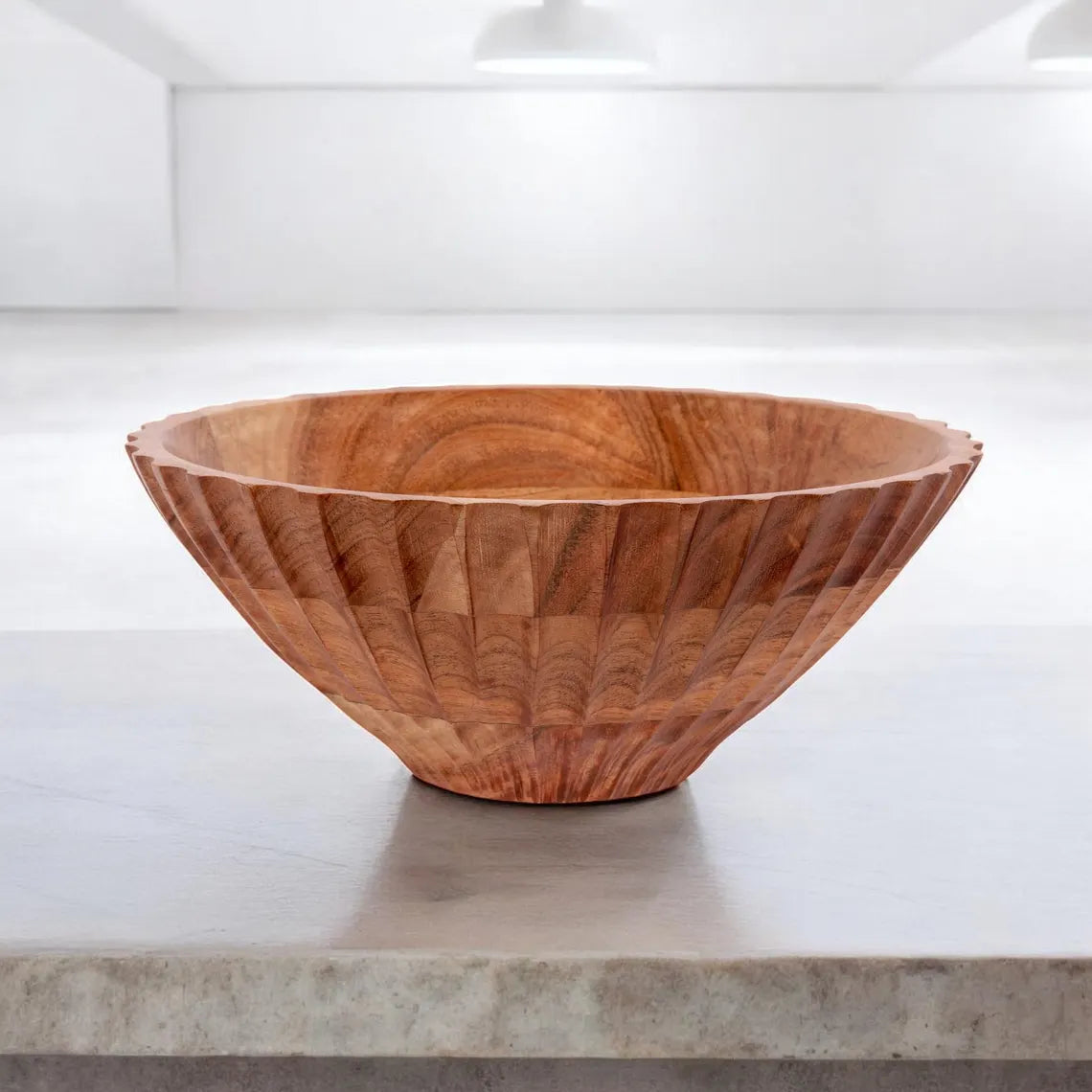 A large, fluted wooden serving bowl with a carved exterior pattern sitting on a concrete countertop.