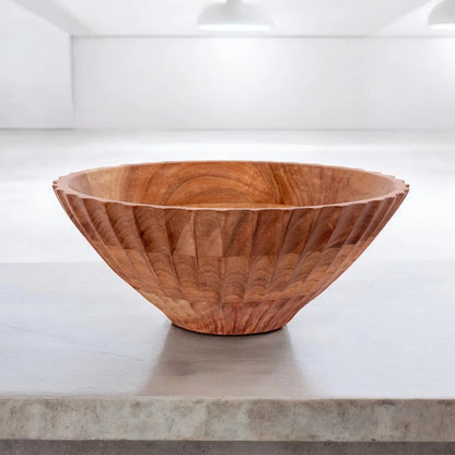 A large, fluted wooden serving bowl with a carved exterior pattern sitting on a concrete countertop.