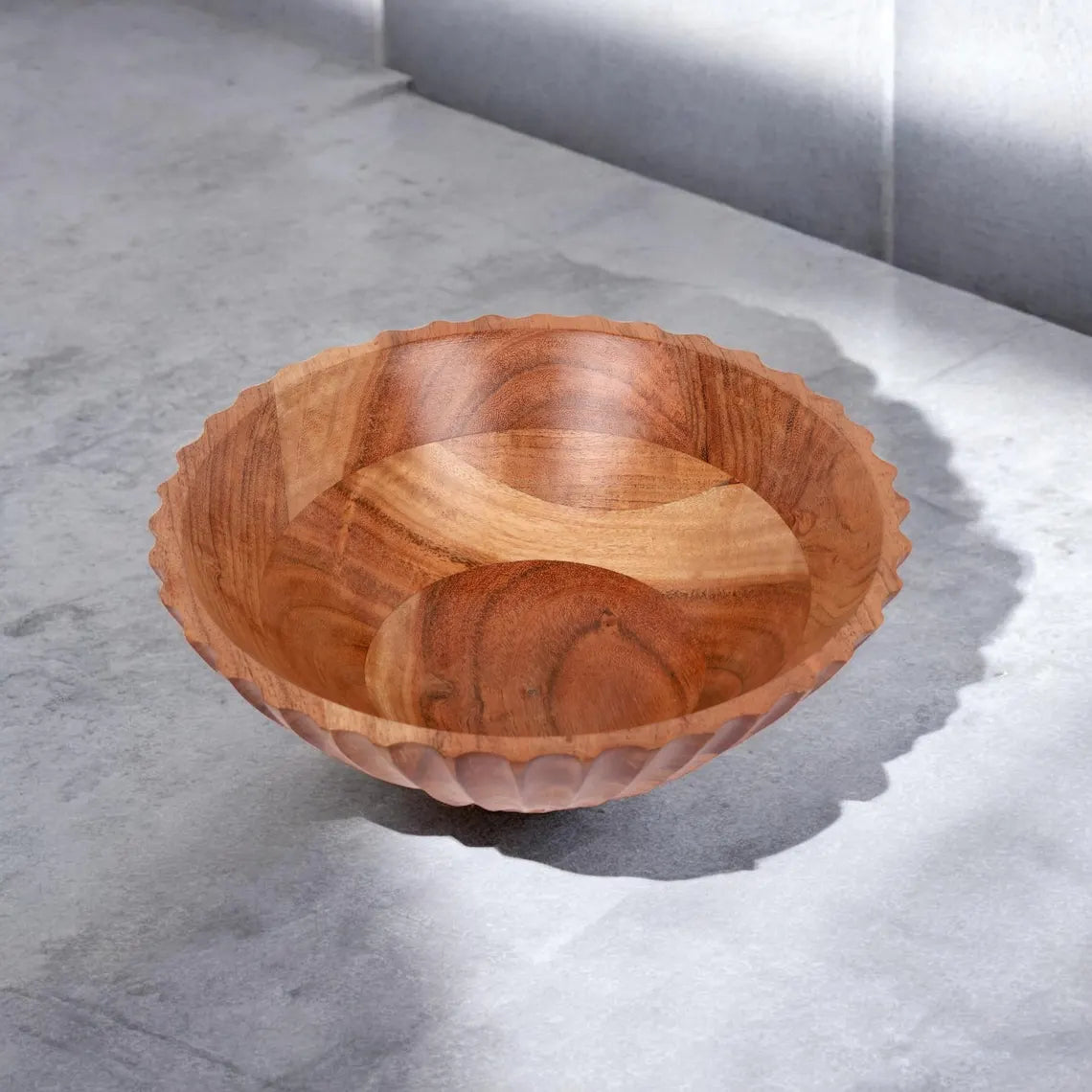 A large, fluted wooden serving bowl with a carved exterior pattern sitting on a concrete countertop.