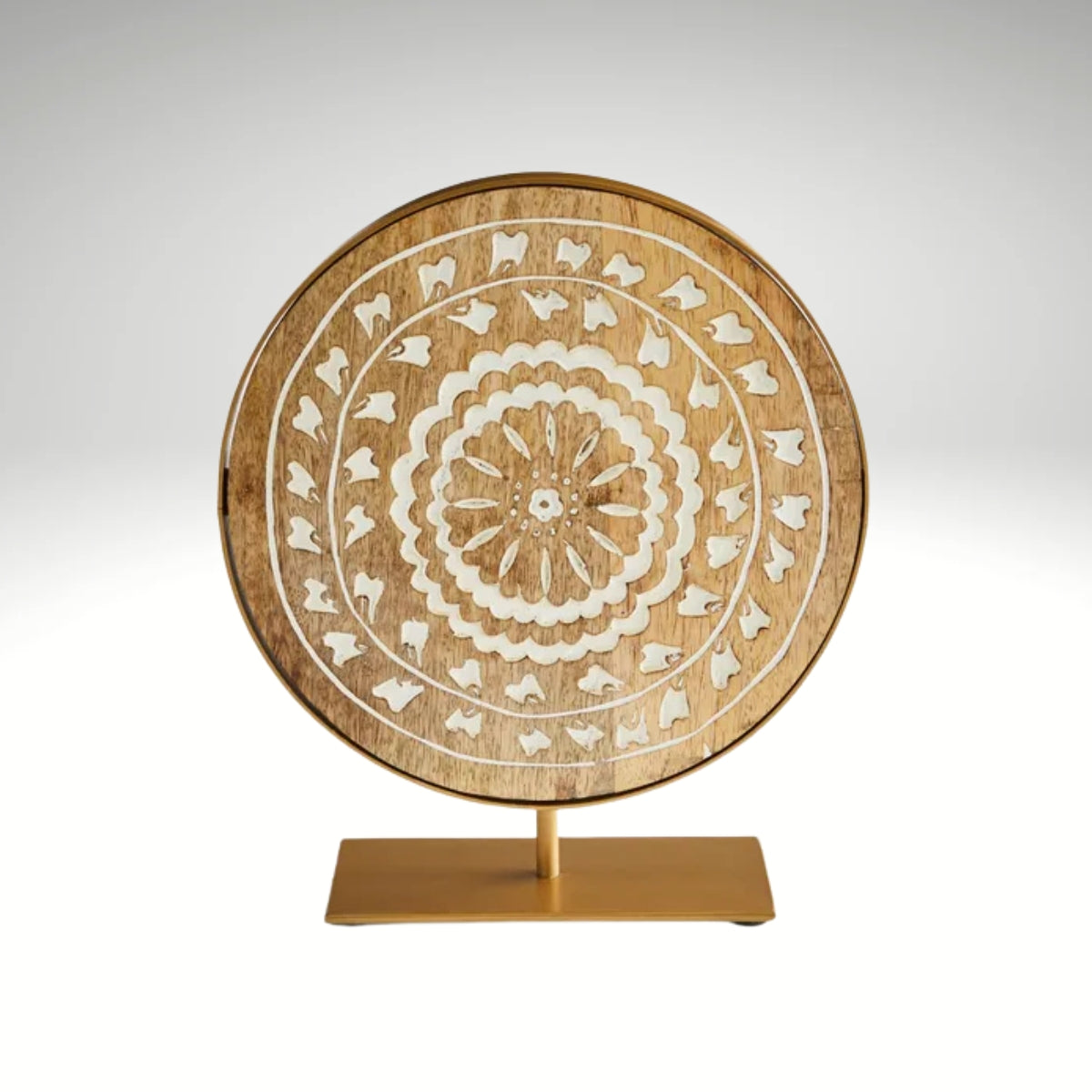 A circular carved mango wood plaque with white concentric floral patterns, mounted on a gold metal stand.