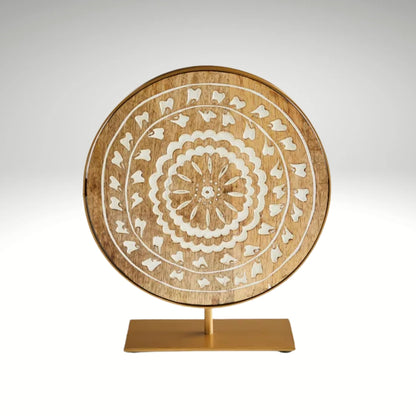 A circular carved mango wood plaque with white concentric floral patterns, mounted on a gold metal stand.