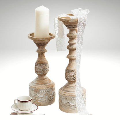 Two vintage-style carved pillar candle holders on a table, one holding a white candle.