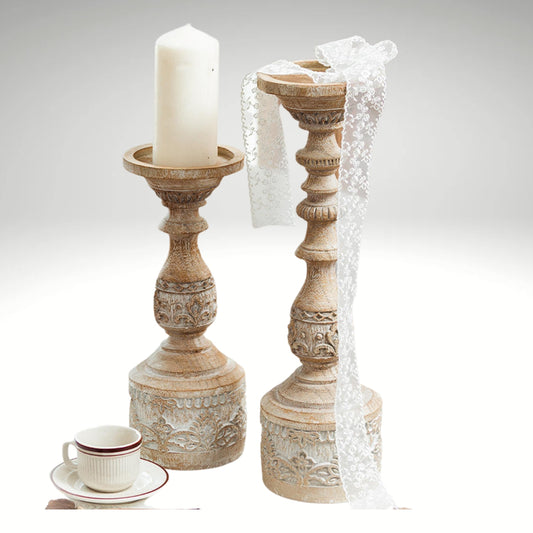 Two vintage-style carved pillar candle holders on a table, one holding a white candle.