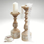 Two vintage-style carved pillar candle holders on a table, one holding a white candle.