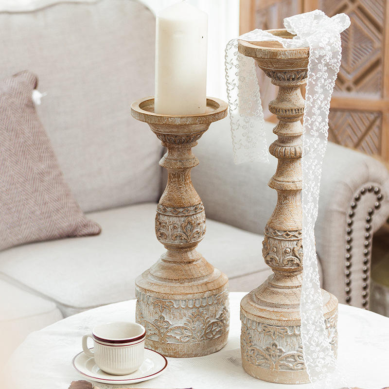 Two vintage-style carved pillar candle holders on a table, one holding a white candle.