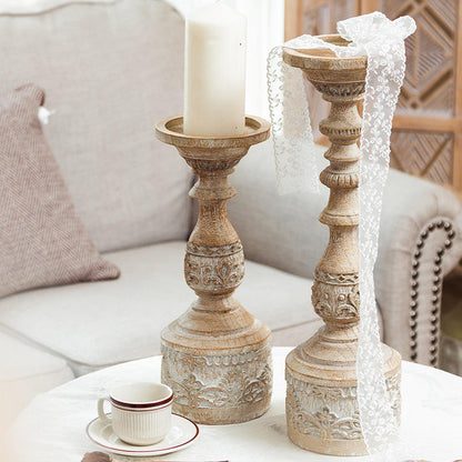 Two vintage-style carved pillar candle holders on a table, one holding a white candle.