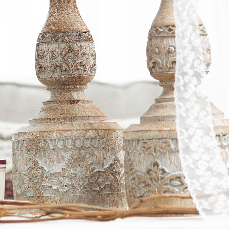 Two vintage-style carved pillar candle holders on a table, one holding a white candle.