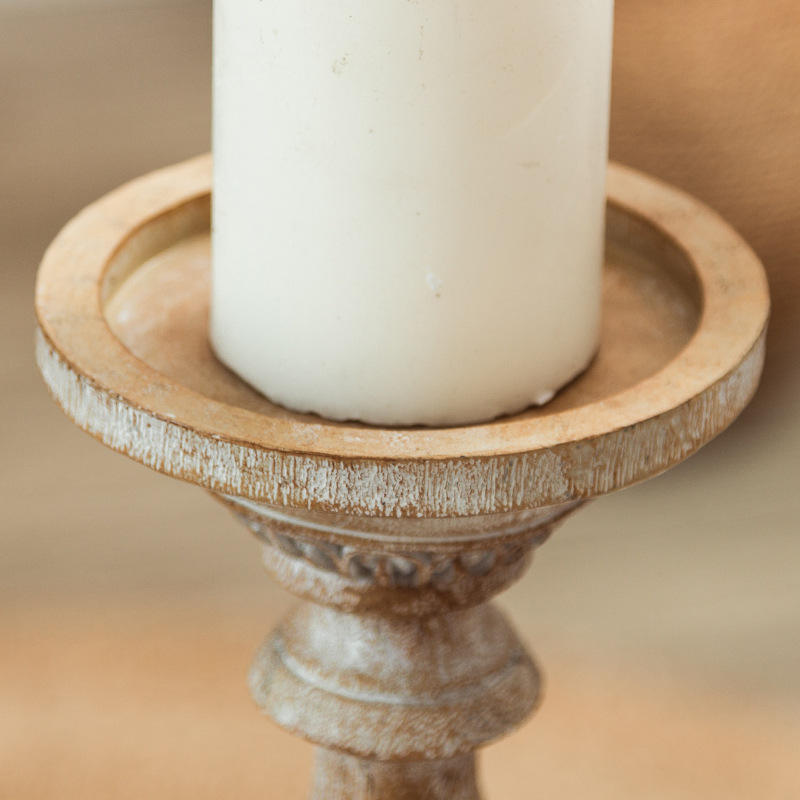 Two vintage-style carved pillar candle holders on a table, one holding a white candle.