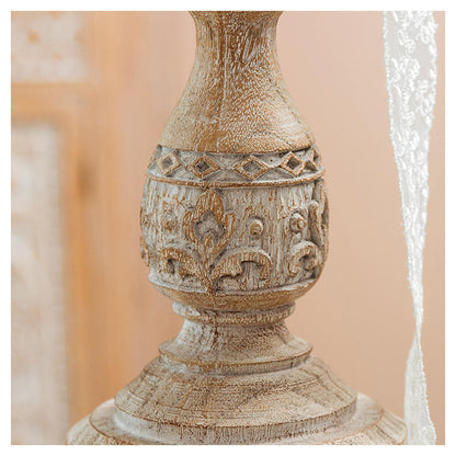 Two vintage-style carved pillar candle holders on a table, one holding a white candle.