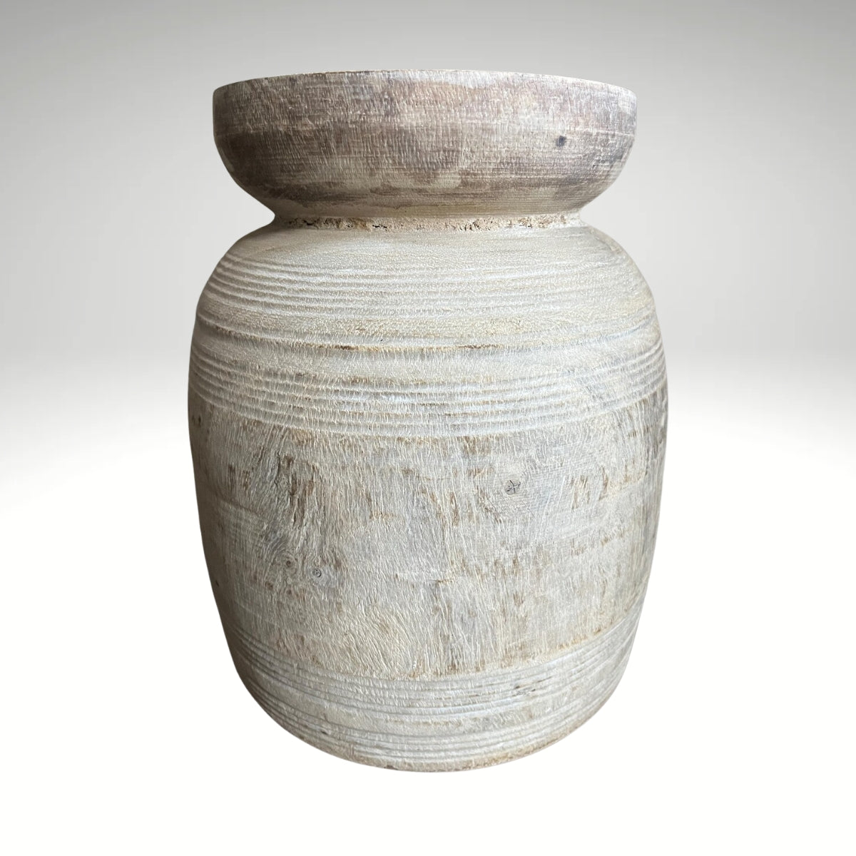 A rustic, light-colored wooden vase with a textured, ribbed surface and a natural wood rim sitting on a dark surface.