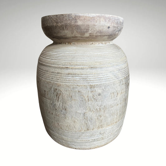 A rustic, light-colored wooden vase with a textured, ribbed surface and a natural wood rim sitting on a dark surface.
