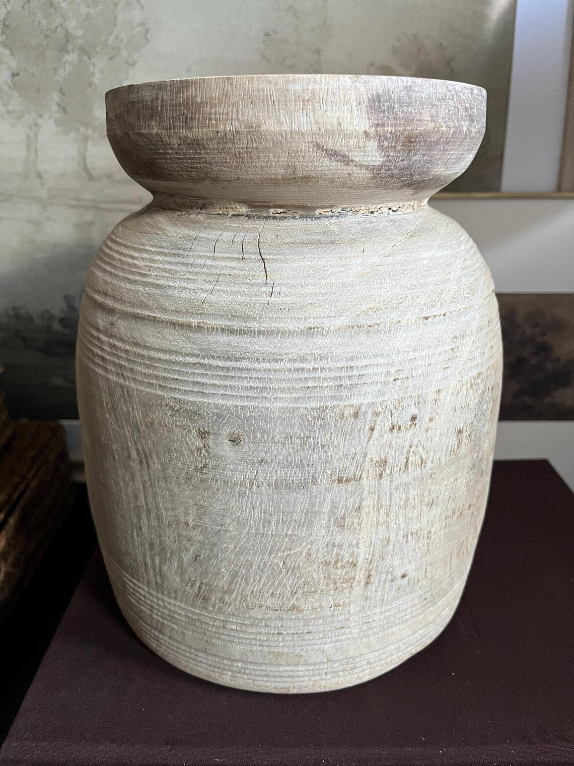 A rustic, light-colored wooden vase with a textured, ribbed surface and a natural wood rim sitting on a dark surface.