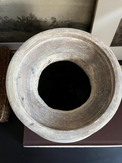 A rustic, light-colored wooden vase with a textured, ribbed surface and a natural wood rim sitting on a dark surface.