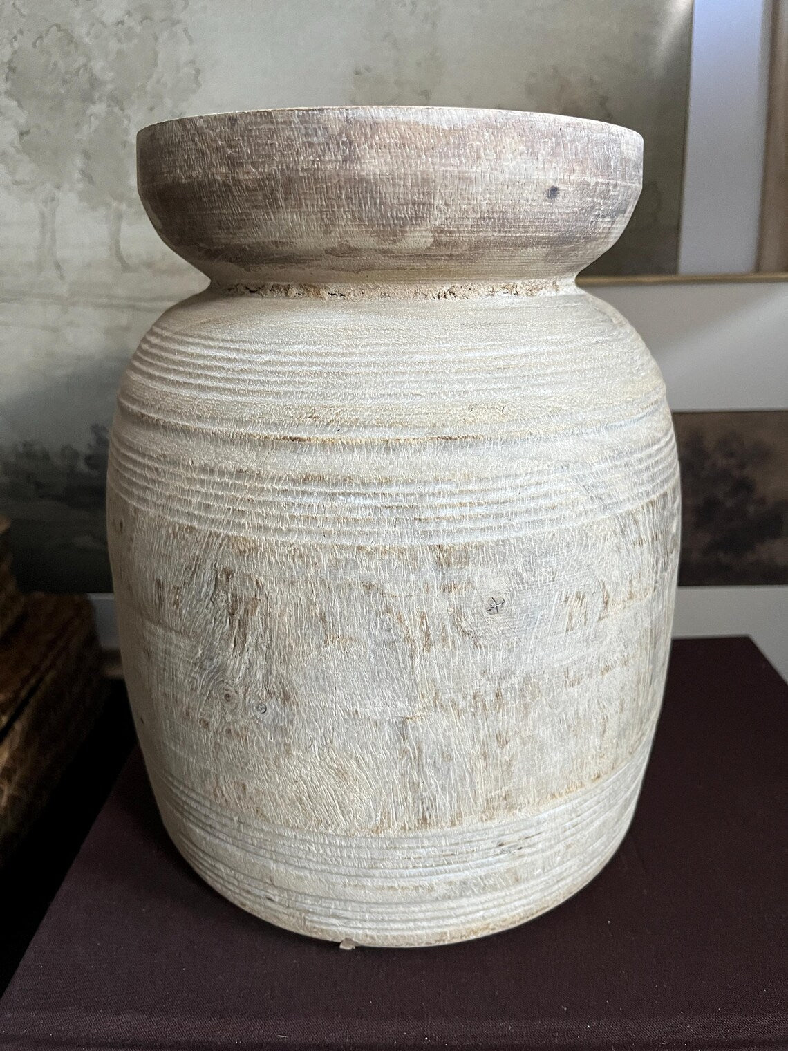 A rustic, light-colored wooden vase with a textured, ribbed surface and a natural wood rim sitting on a dark surface.