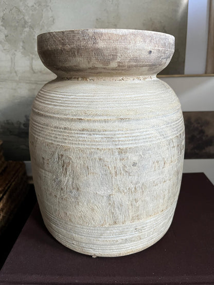 A rustic, light-colored wooden vase with a textured, ribbed surface and a natural wood rim sitting on a dark surface.