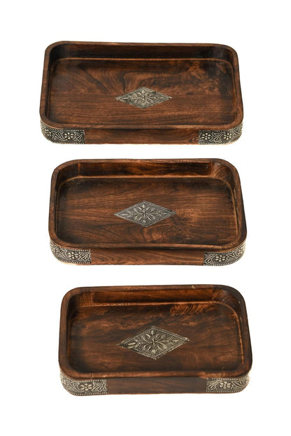 A stack of three rectangular dark brown wooden serving trays featuring ornate metal diamond inlays in the center and decorative metal borders along the corners.