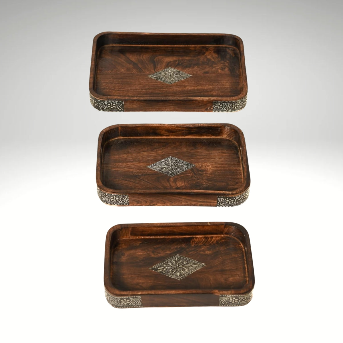 A stack of three rectangular dark brown wooden serving trays featuring ornate metal diamond inlays in the center and decorative metal borders along the corners.