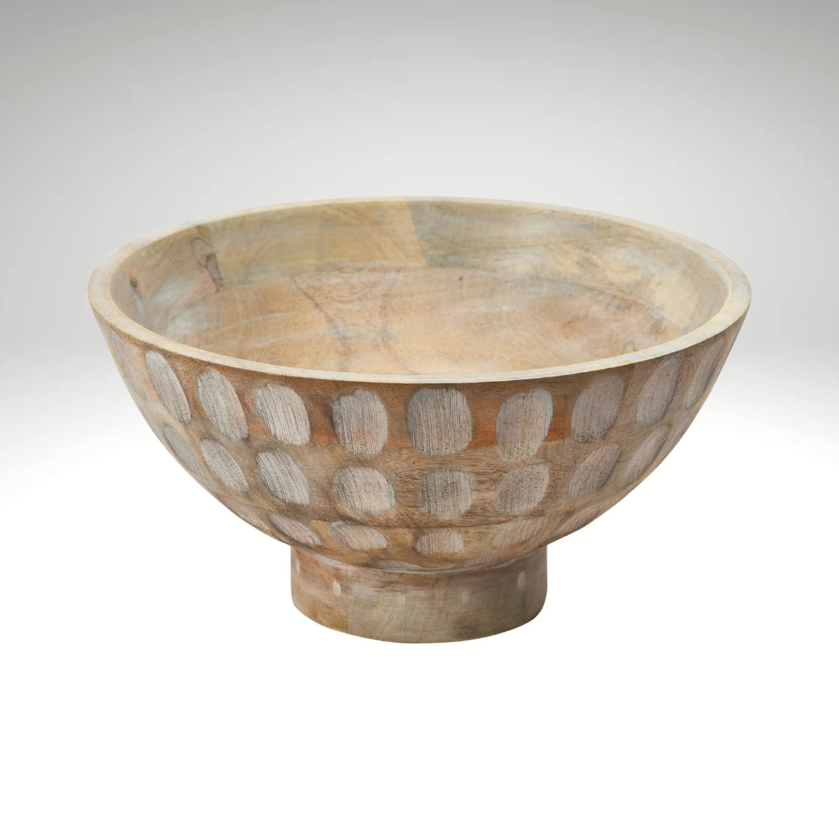 A round, natural mango wood bowl with a footed base and a carved, circular pattern decorating the outer surface.