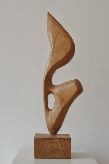 An abstract biomorphic wood sculpture with smooth curves and a hollow cutout, mounted on a square wooden base.