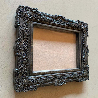  An ornate, dark brown antique-style photo frame with intricate floral carvings 