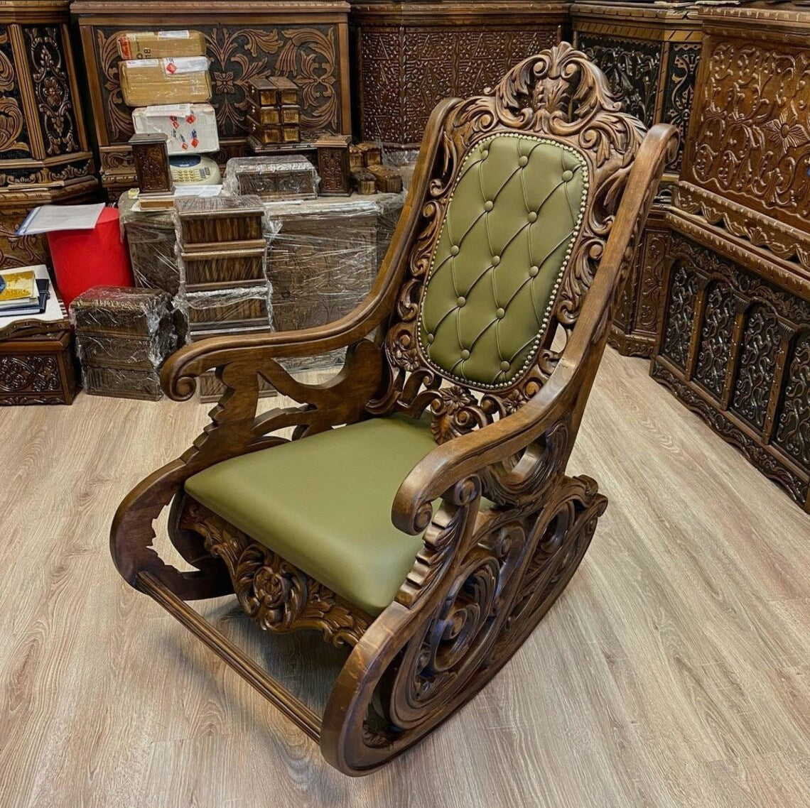 Vintage-style wooden rocking chair with intricate carvings and green cushioned upholstery.