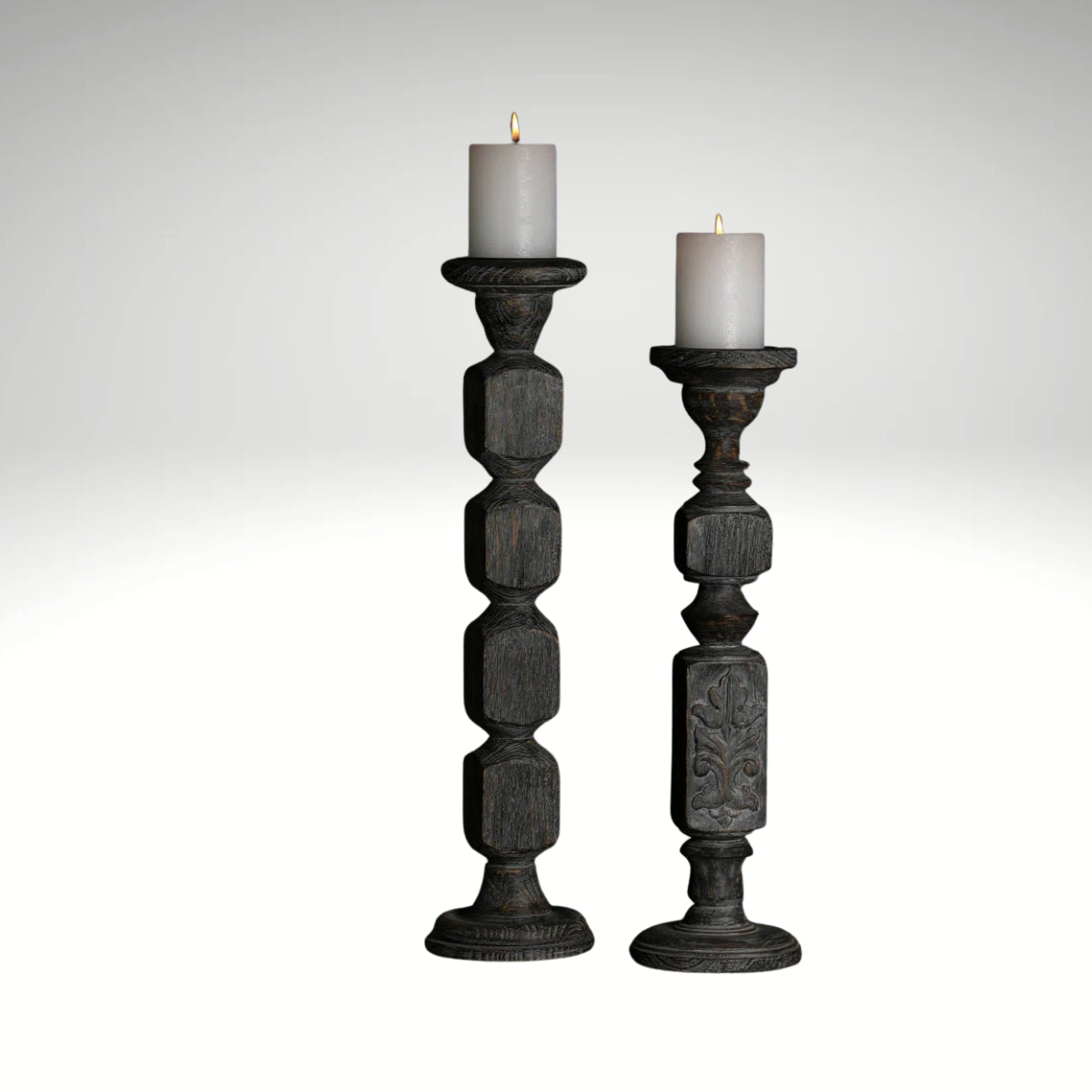 A pair of tall, hand-carved wooden pillar candle holders with a distressed black finish