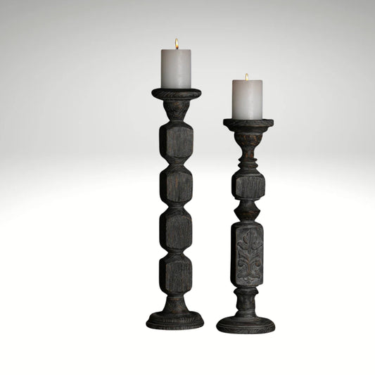 A pair of tall, hand-carved wooden pillar candle holders with a distressed black finish