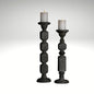 A pair of tall, hand-carved wooden pillar candle holders with a distressed black finish