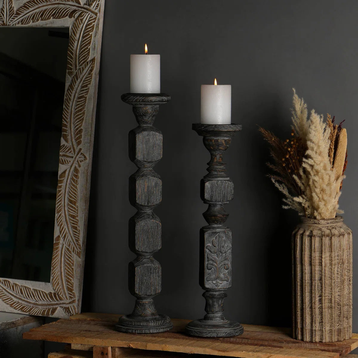 A pair of tall, hand-carved wooden pillar candle holders with a distressed black finish