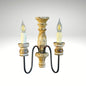 A vintage-style double wall sconce with a distressed carved wooden body, curved black metal arms, and two faux-candle LED bulbs.