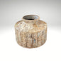A short, wide ceramic vase featuring textured, block-stamped relief patterns in off-white and beige earthy tones.