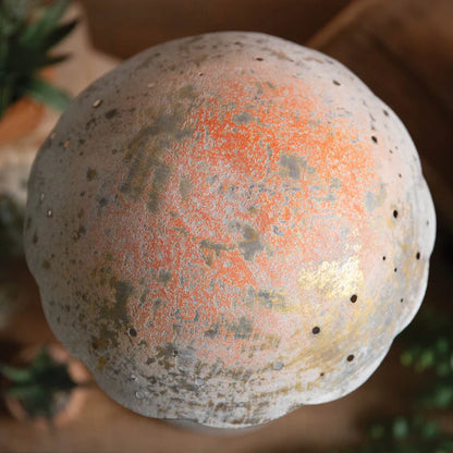 A rustic, mushroom-shaped decorative piece with a textured light-colored finish and golden highlights, placed on a wooden table alongside potted
