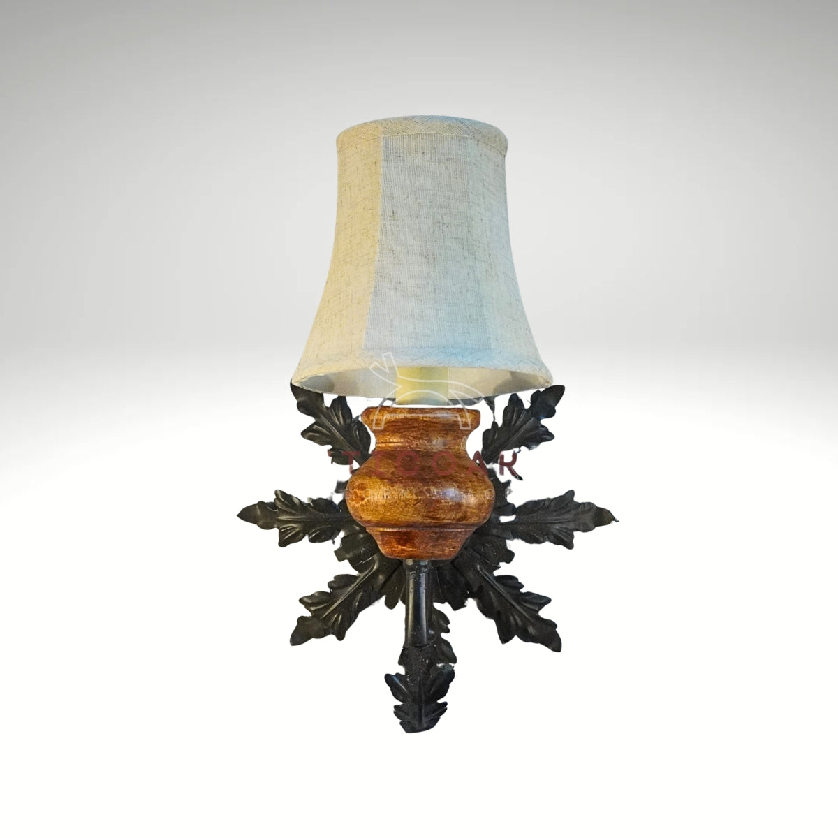 A wall-mounted light fixture featuring a beige fabric shade, a polished wooden base, and a black wrought iron backplate shaped like oak leaves.
